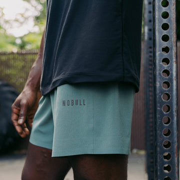 Person wearing green shorts with 'NOBULL' logo outdoors