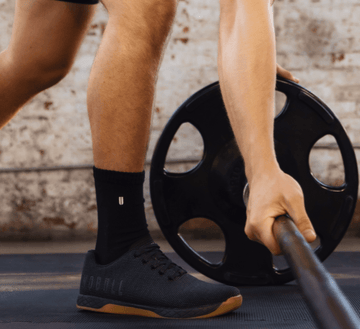 Man wearing Outwork shoes picking up barebell.