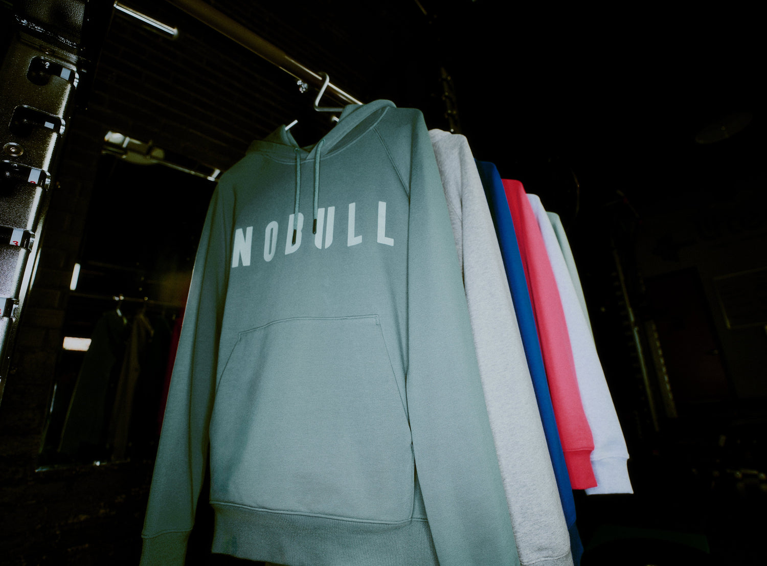Green hoodie with 'NOBULL' text hanging on a rack against a dark background