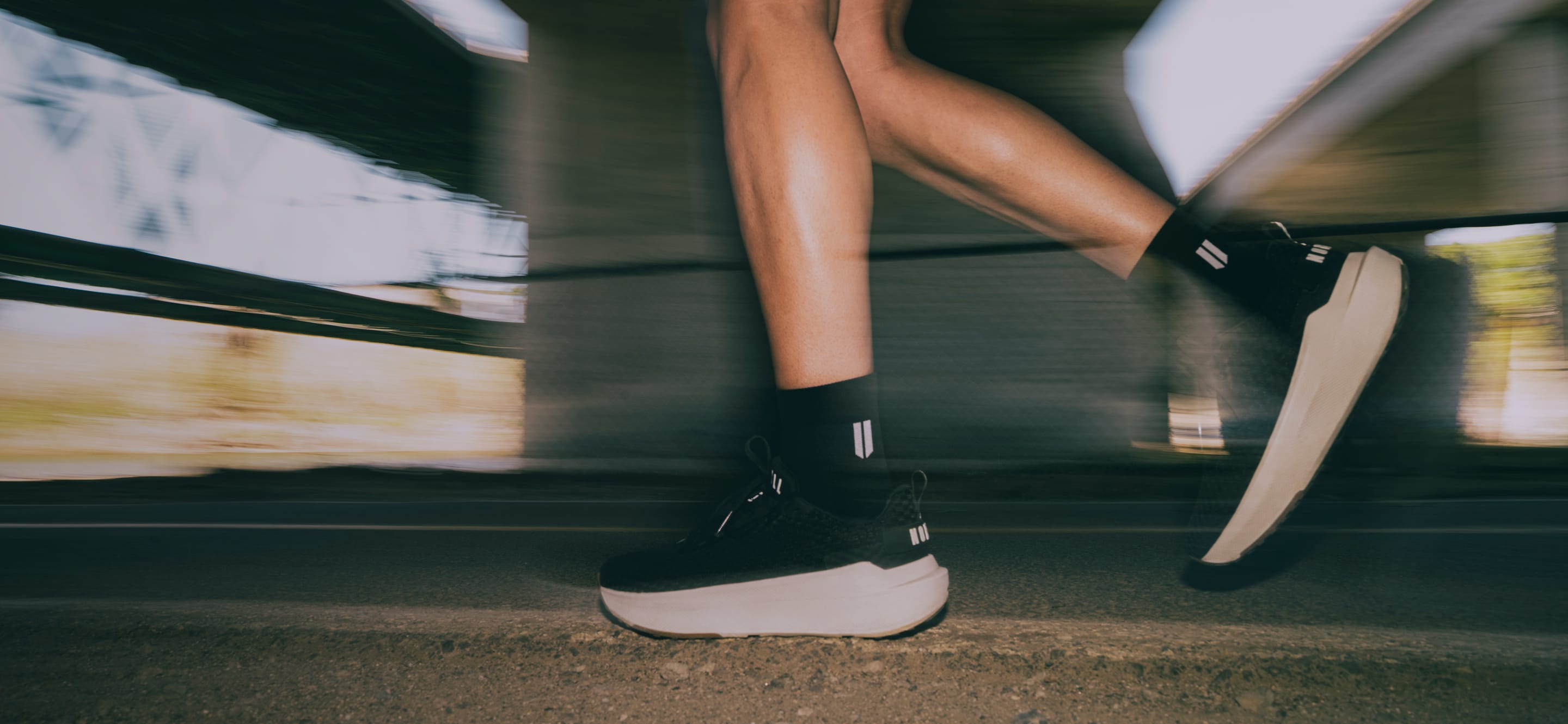 Person wearing black sneakers with white soles on a blurred outdoor background