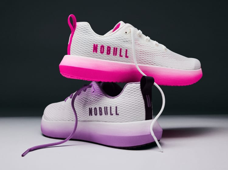 product - A pair of white athletic sneakers with a vibrant gradient sole, stacked with one shoe on top of the other. The top shoe features a hot pink gradient sole and heel pull tab, while the bottom shoe has a purple gradient sole and heel pull tab.