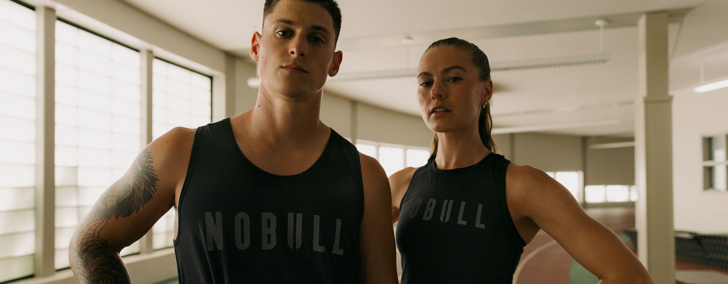 Two people wearing NOBULL tank tops in a gym setting.