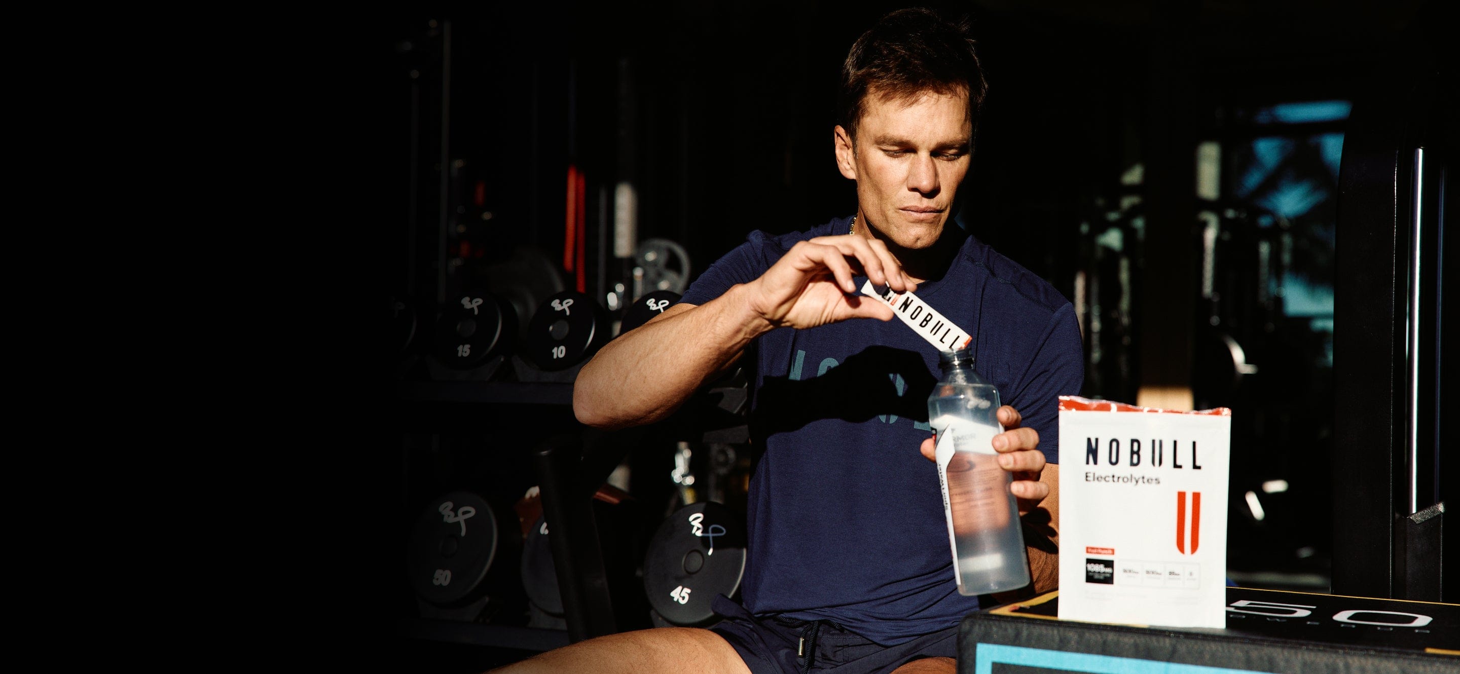 Tom Brady pouring NOBULL electrolytes into a water bottle.