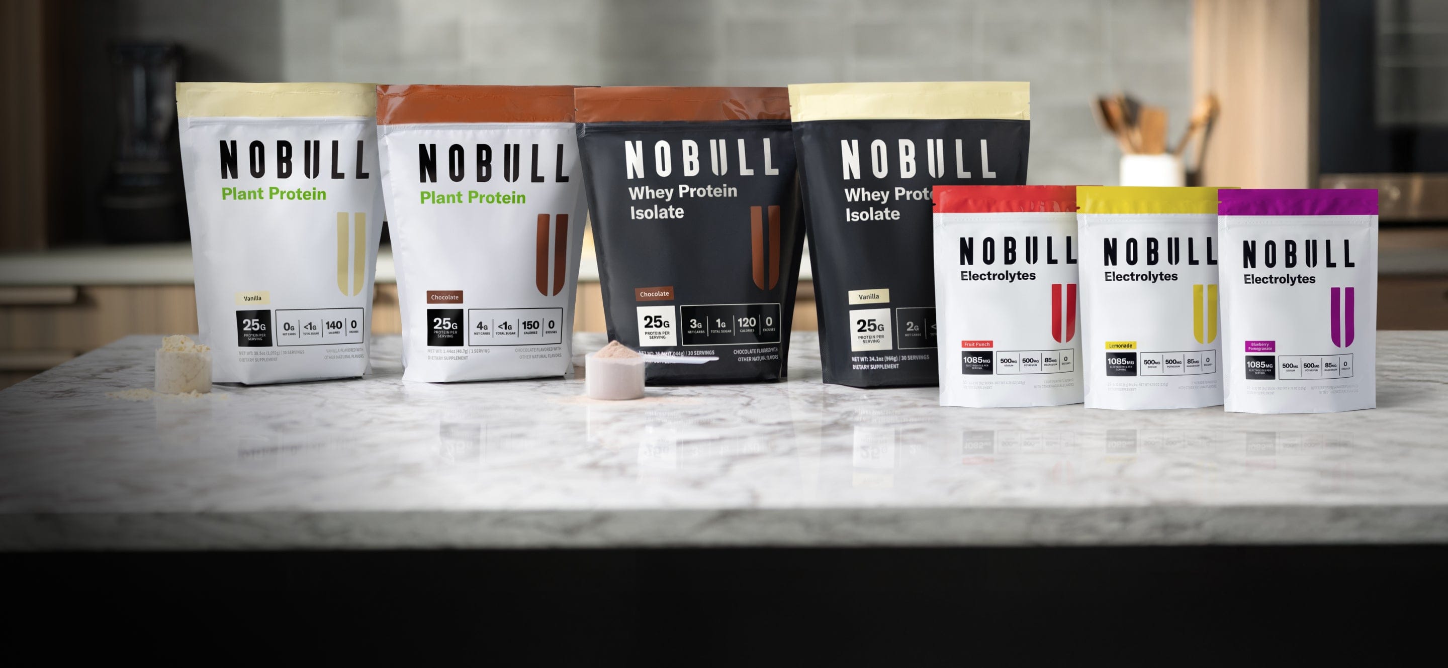 Assorted packages of NOBULL nutrition products on a kitchen counter.