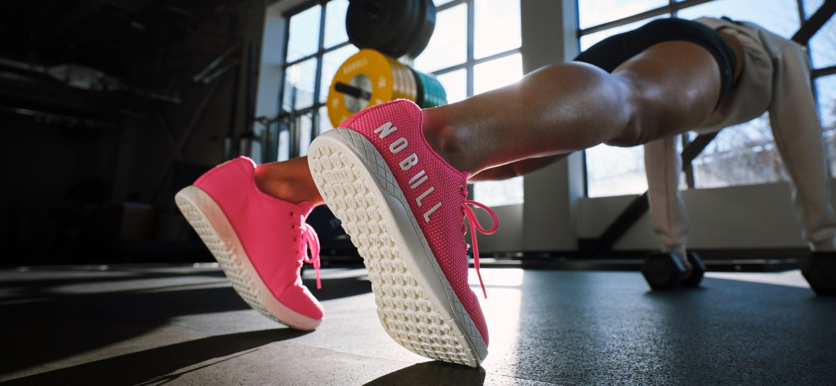 Person exercising with pink 'NOBULL' sneakers on a gym floor.