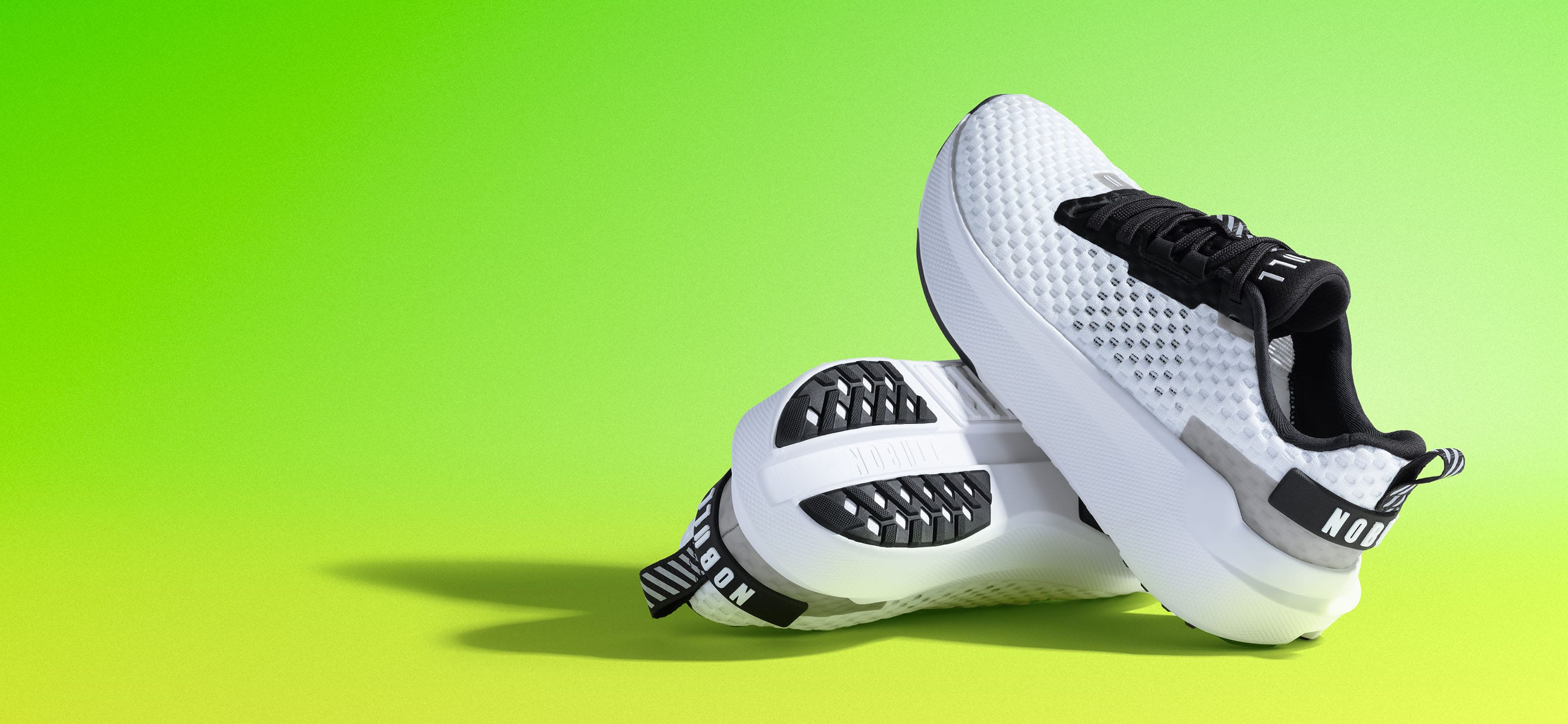 product - A pair of white and black NOBULL Journey 2 shoes with a textured mesh upper and thick white platform soles, displayed against a bright lime green gradient background.