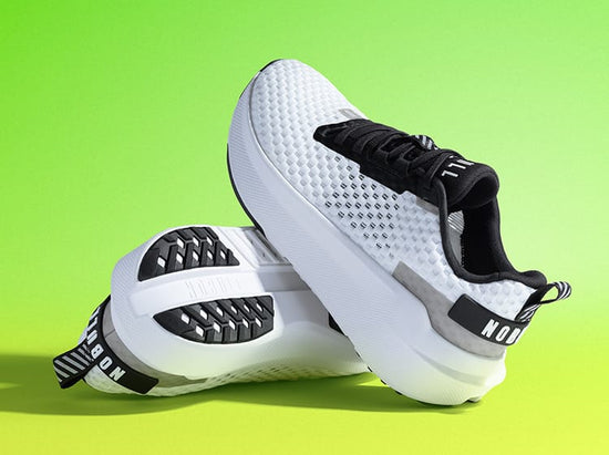 product - A pair of white and black NOBULL Journey 2 shoes with a textured mesh upper and thick white platform soles, displayed against a bright lime green gradient background.