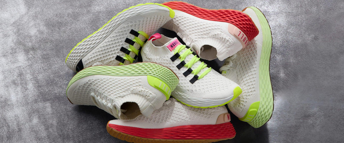 Promo - A pile of white athletic sneakers with bright neon green, red, and black details, arranged on a textured gray surface.