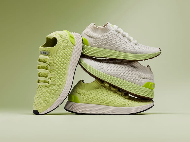 promo - Allday Knit Shoes in a stacked studio arrangement on a soft green background. The shoes feature a textured knit upper in light lime green and white, with a thick white midsole and small neon green accents.