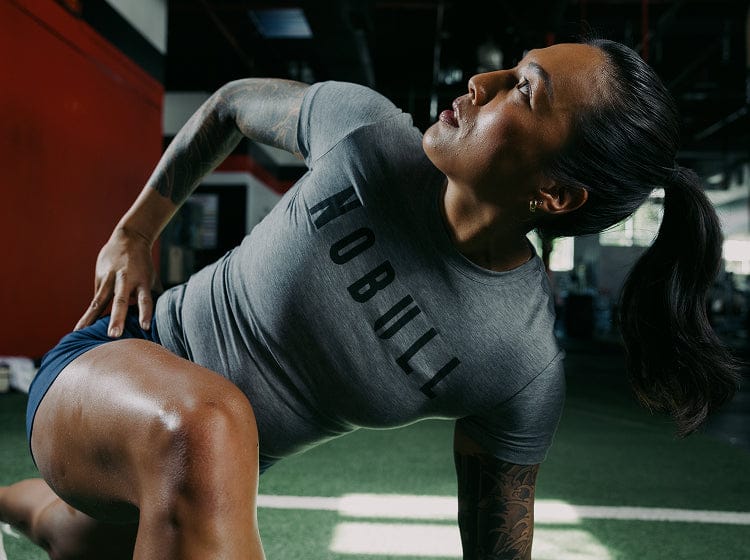 Person exercising in a gym wearing a gray NOBULL tee.