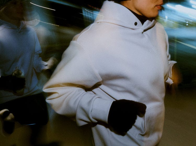 Person wearing a white hoodie and black gloves in a blurred indoor setting