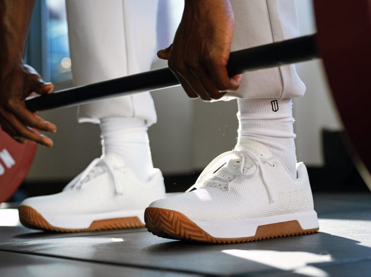 White Outwork Edge Shoes with brown soles worn by a person lifting weights.