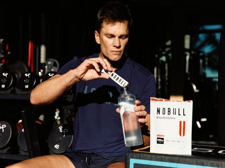 Tom Brady pouring NOBULL electrolytes into a water bottle.
