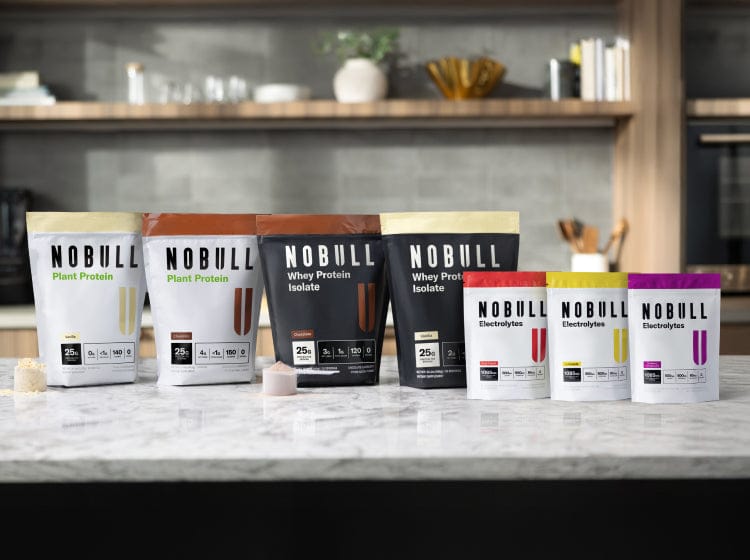 Assorted packages of NOBULL nutrition products on a kitchen counter.
