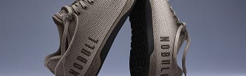 A pair of light gray knit athletic shoes with black soles, shown from a low angle against a dark blue-gray gradient background.