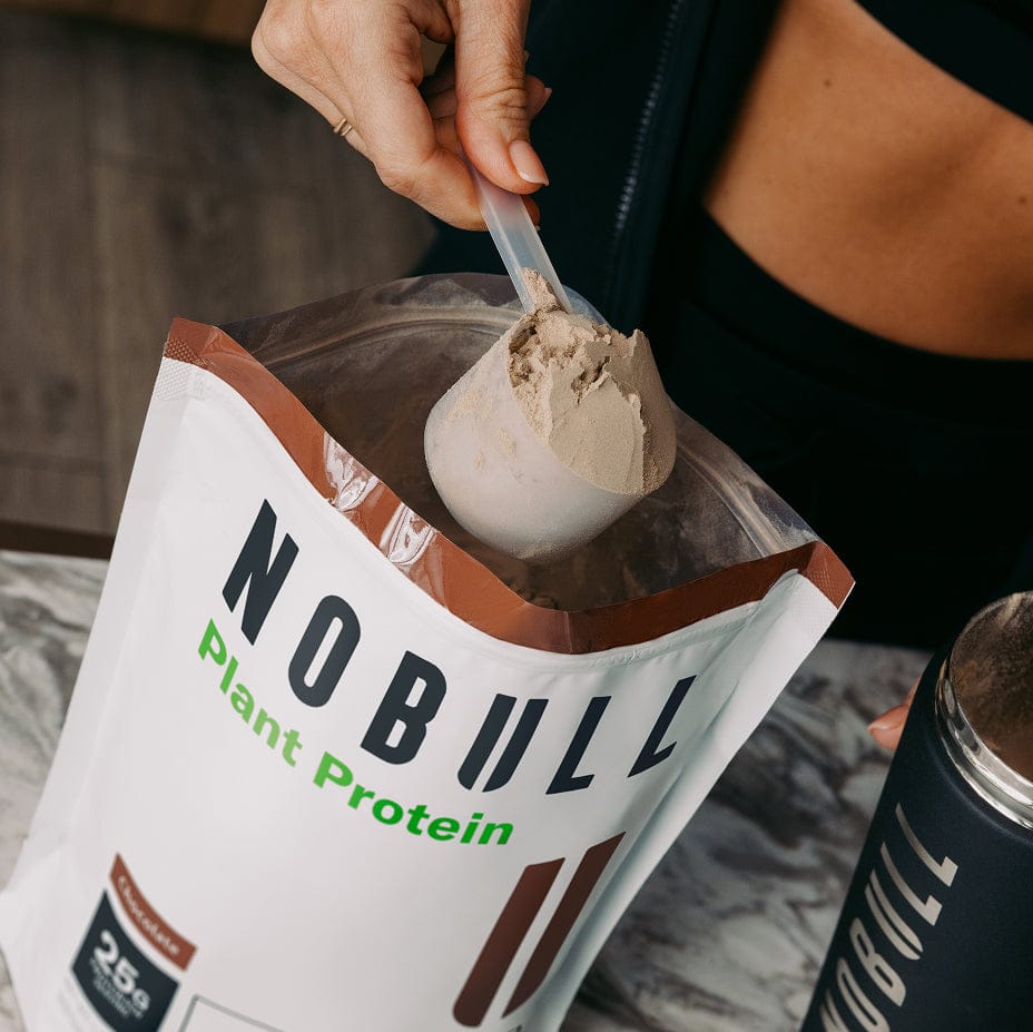 Person scooping NOBULL Plant Protein into a container with packaging visible.