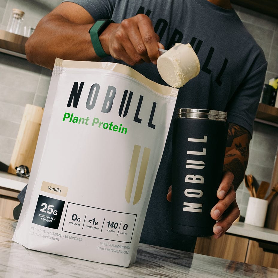 Person holding a Vanilla NOBULL plant protein package and container in a kitchen.