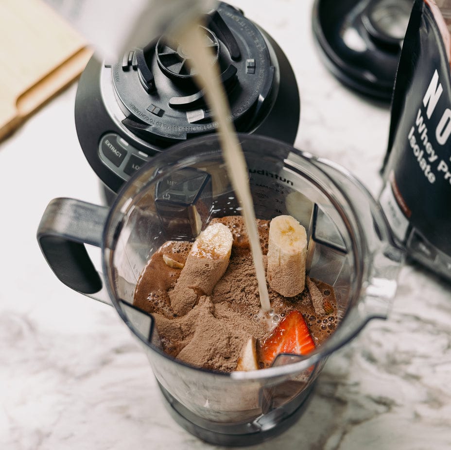 Blender with ingredients being poured into it on a marble surface