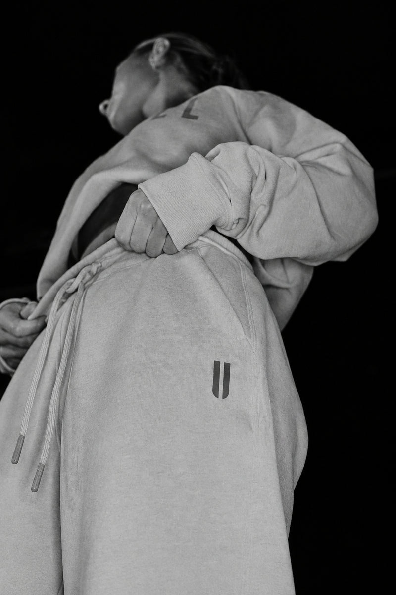 A person wearing a mint green hoodie and matching sweatpants, shown from the back against a solid black background. The hoodie has a small dark gray double vertical bar logo on the left side of the back pocket area.