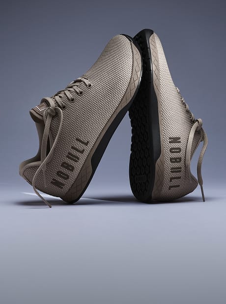 A pair of athletic sneakers in a taupe-beige mesh and synthetic composite material, shown from the side and sole views against a dark gray studio background.