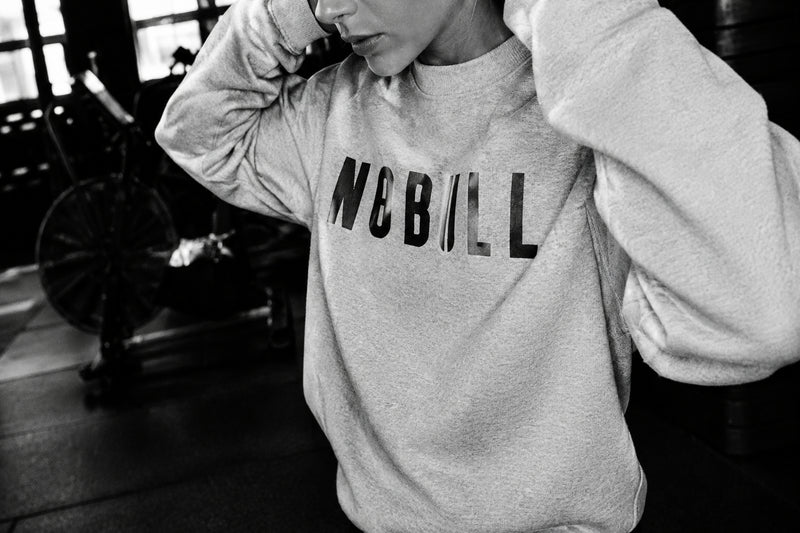 A person wearing a light mint green sweatshirt with a dark gray graphic print that reads 'MIBILI' on the chest, photographed in a gym setting with exercise equipment in the background.