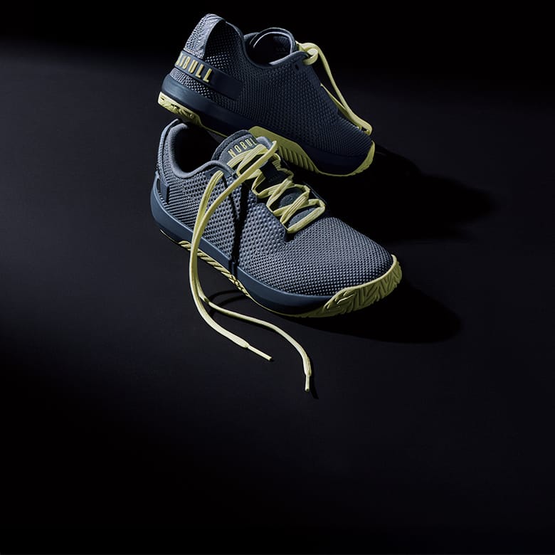 Product - A pair of athletic sneakers in dark navy blue mesh with lime green laces, outsole accents, and branding, displayed on a dark reflective surface.