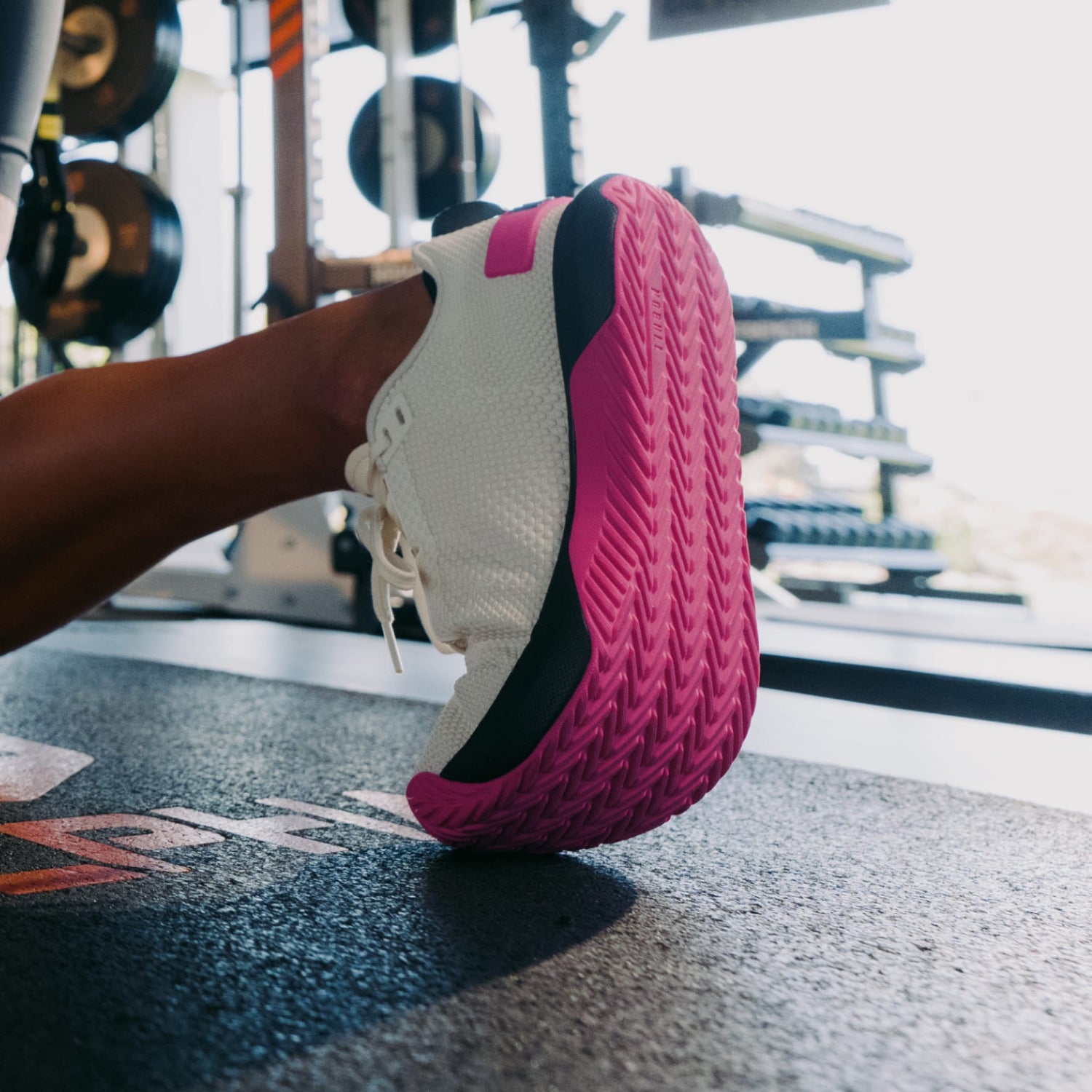 Close-up of a pink and white athletic shoe on a gym floor with weights in the background