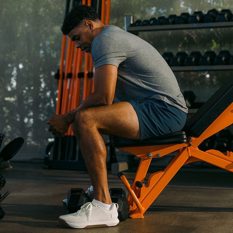 Buy, More Save More Promotion featuring a Model in a gym wearing dark athletic shorts, a gray top, and white sneakers, captured mid-motion in a low plank or sprinting pose with exercise equipment visible in the background.