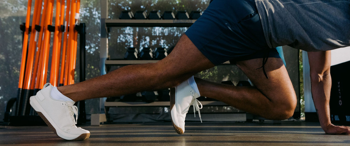 Buy, More Save More Promotion featuring a Model in a gym wearing dark athletic shorts, a gray top, and white sneakers, captured mid-motion in a low plank or sprinting pose with exercise equipment visible in the background.