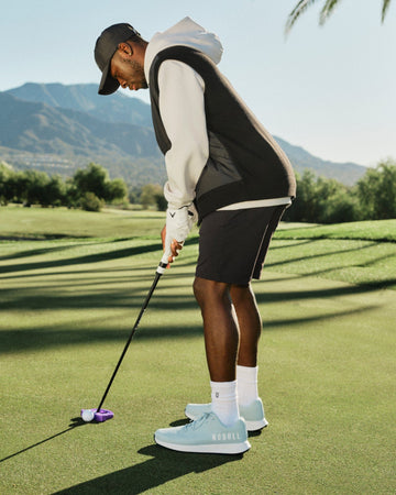 Man playing golf on a green course with mountains in the background