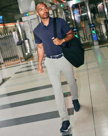 Man in a blue shirt and gray pants walking through an airport terminal.
