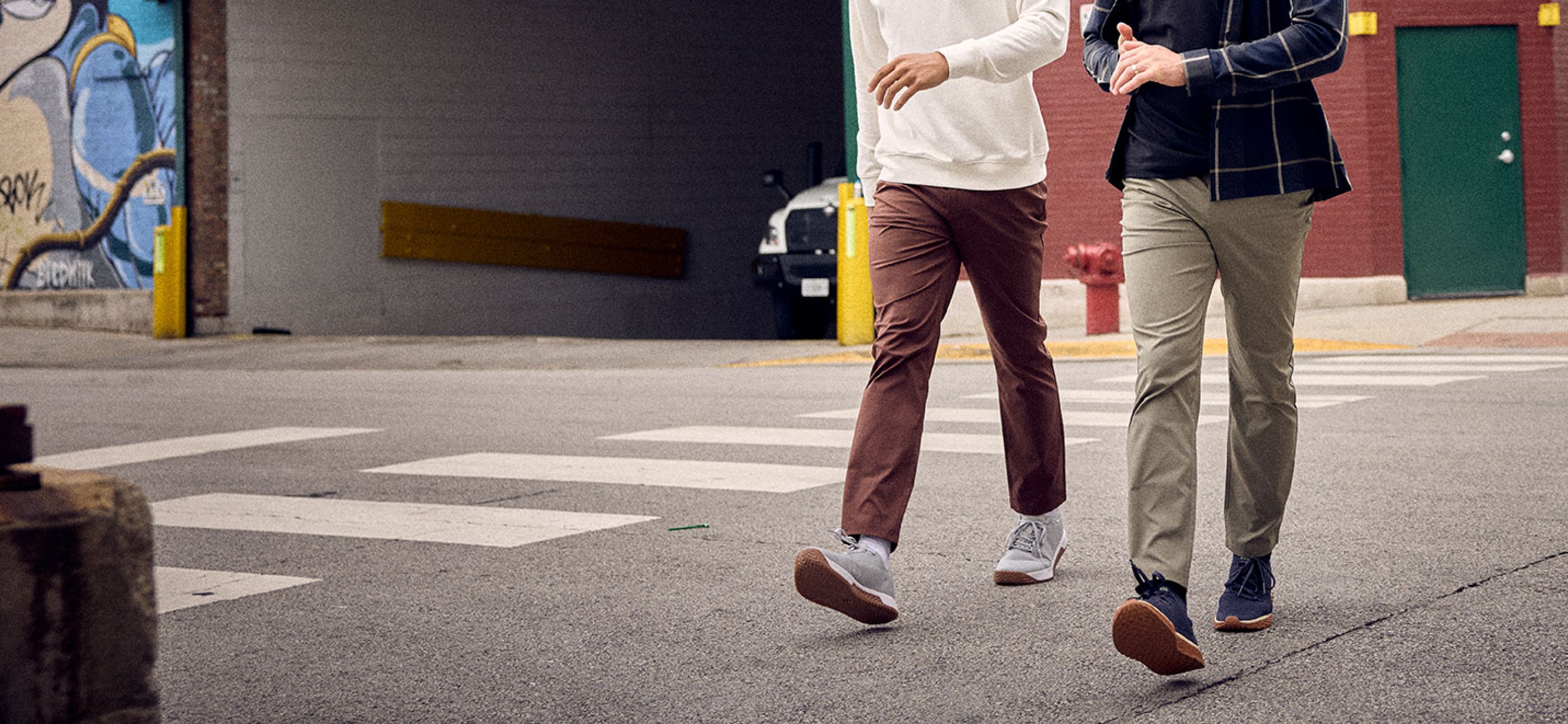 Two people walking on a street with a graffiti-covered wall in the background