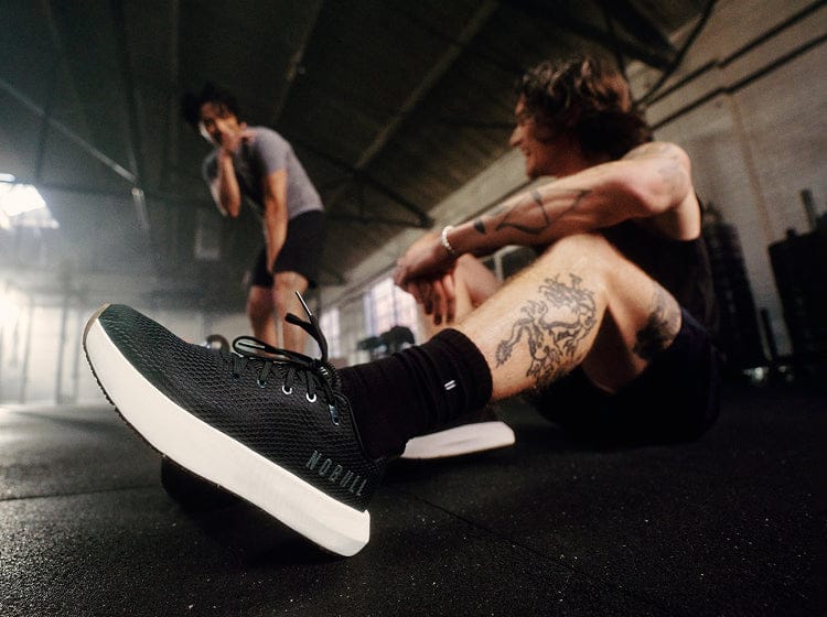 Person sitting on a gym floor wearing black sneakers with white soles, surrounded by gym equipment.
