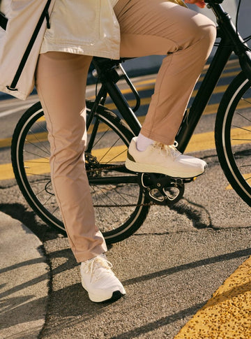 Person riding a bicycle with focus on legs wearing beige pants and white sneakers.