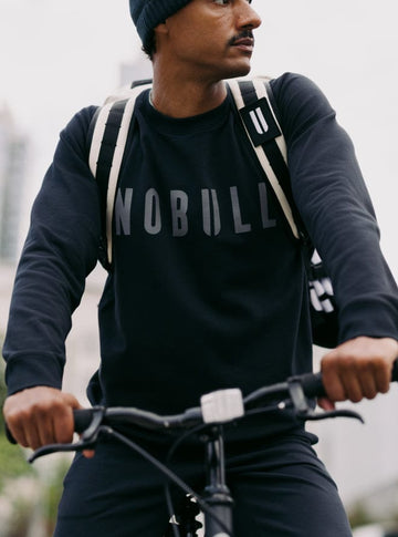 Person riding a bicycle wearing a black sweatshirt with 'NOBULL' text.