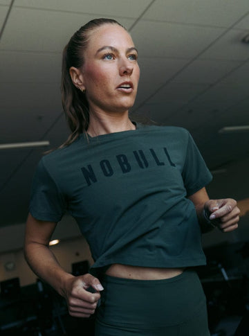 Woman wearing a green 'NOBULL' shirt in an indoor setting