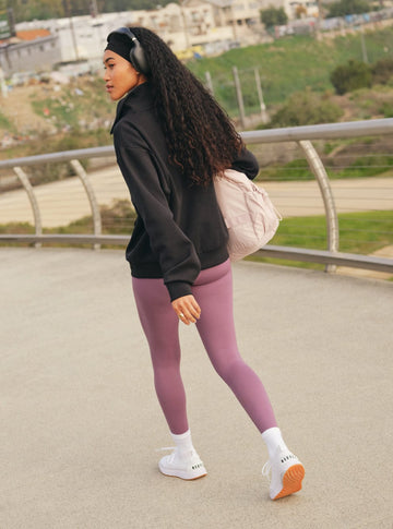 Woman in black hoodie and purple leggings walking outdoors with a scenic background