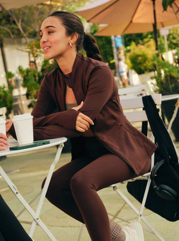 Woman in brown outfit sitting outdoors at a table with a cup.