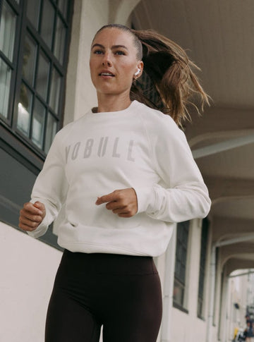 Woman running outdoors wearing a white sweatshirt with visible branding.