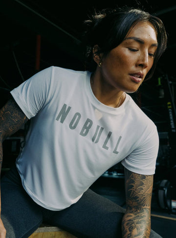 Person wearing a white 'NOBULL' t-shirt in a gym setting