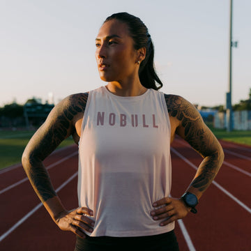 Woman wearing a white tank top with 'NOBULL' text on a running track.