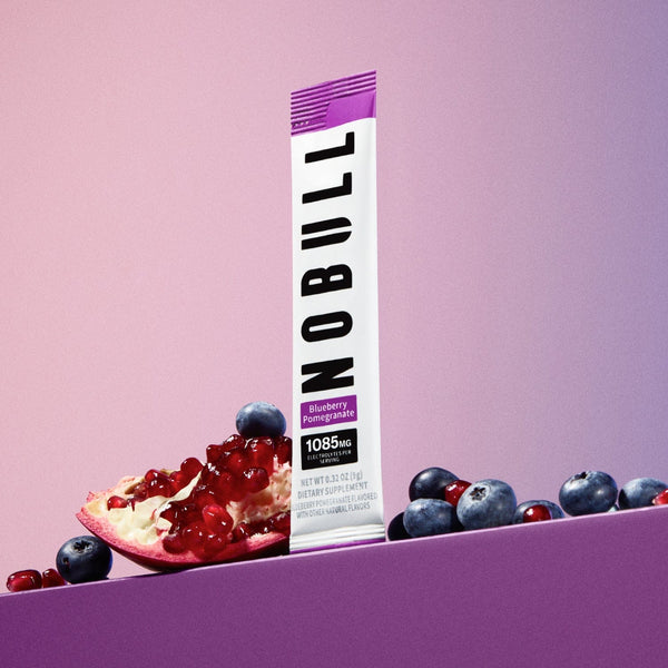 Blueberry Pomegranate NOBULL Electrolyte stick with blueberries and pomegranate on a purple background