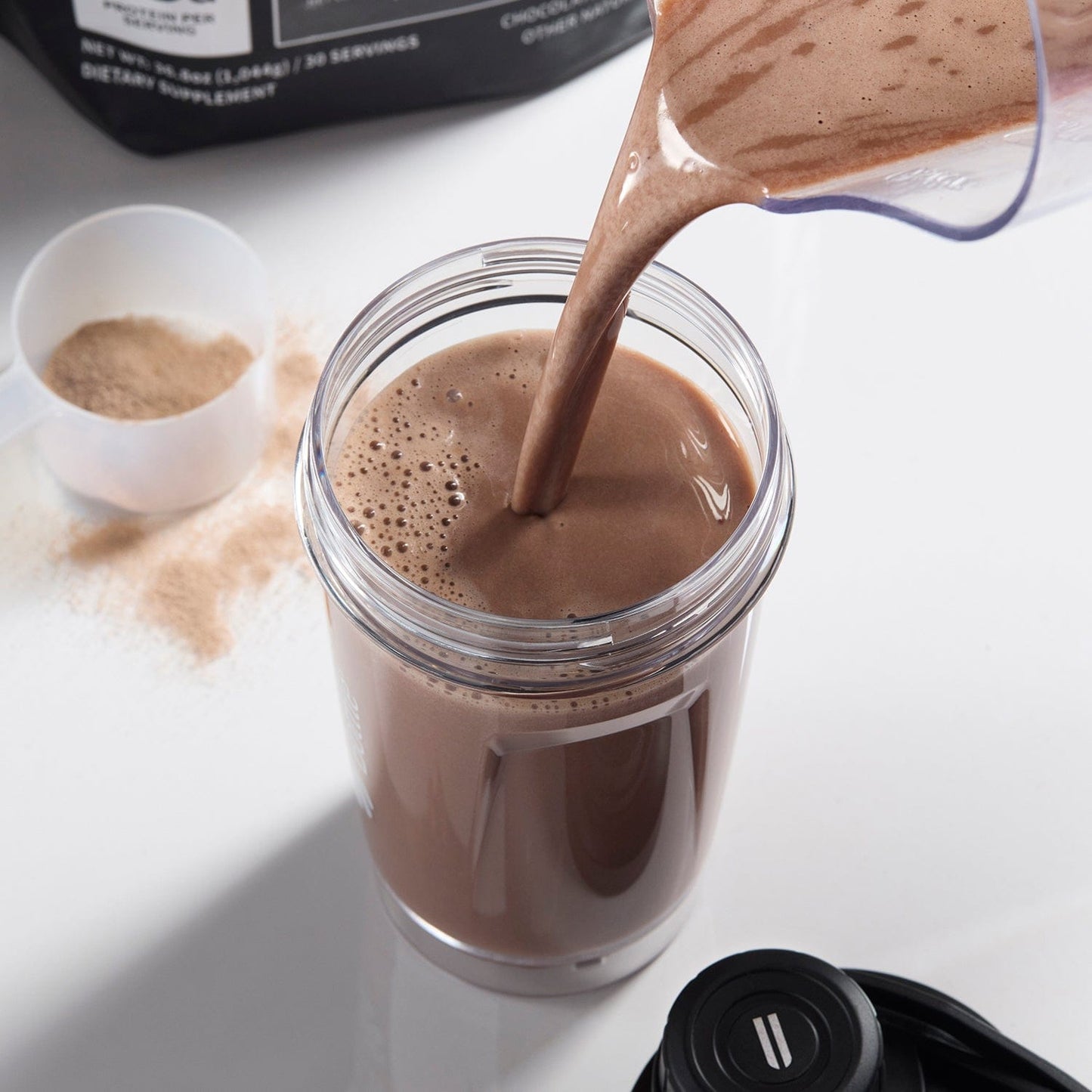 Chocolate powder being poured into a glass jar on a white surface.