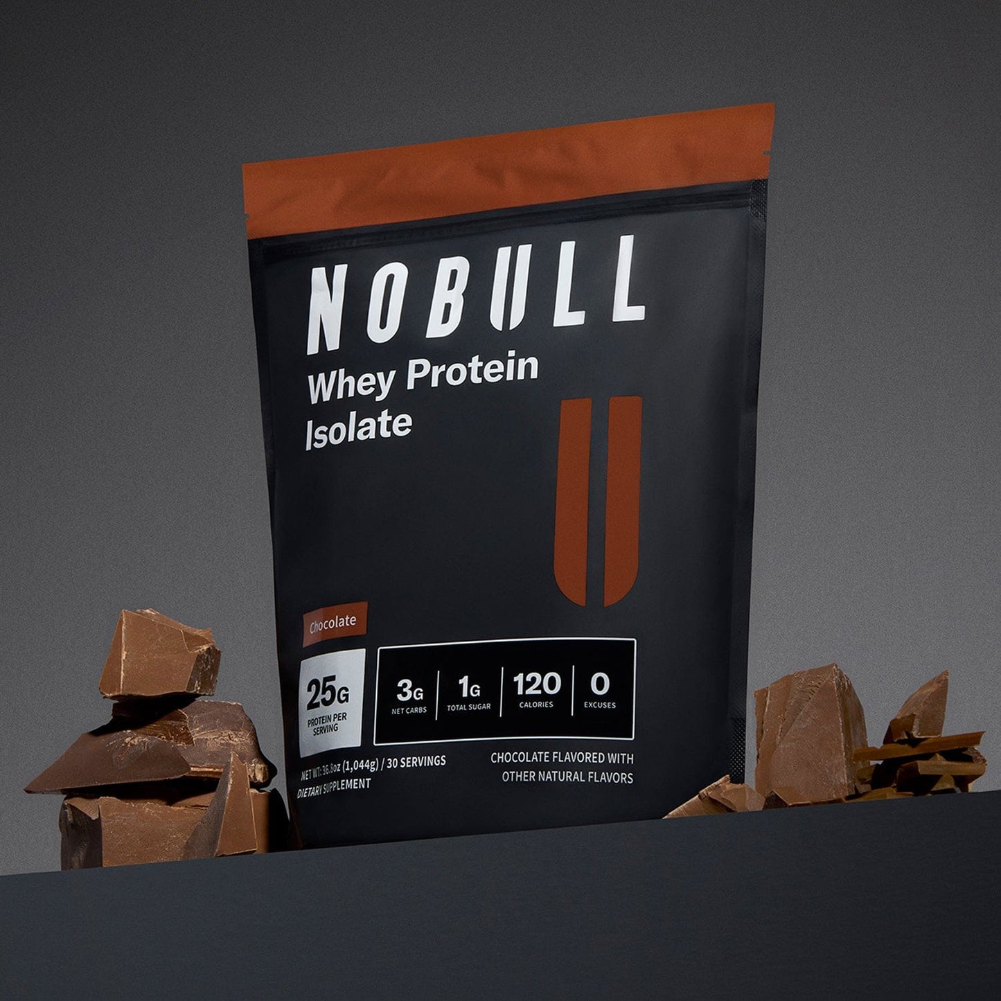 Chocolate NOBULL whey protein isolate package with chocolate pieces on a gray background