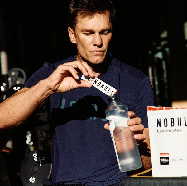Tom Brady pouring an electrolyte stick into a water bottle