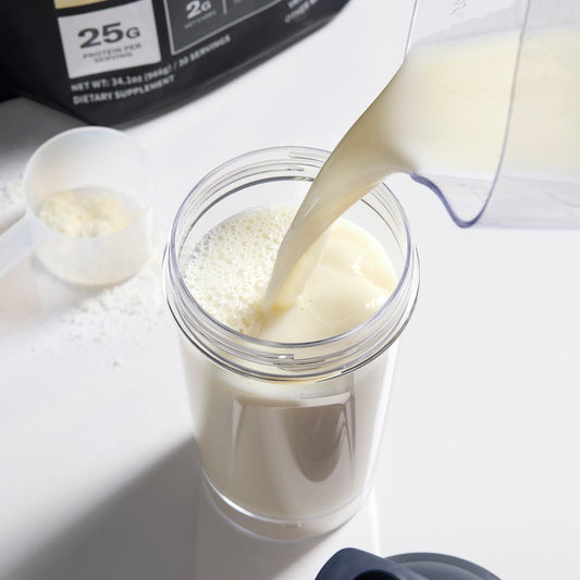 Vanilla Protein powder being poured into a container with a scoop and packaging in the background.